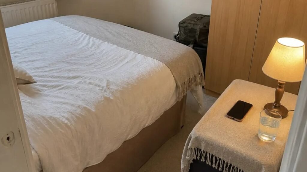 Large suitcase hidden under a throw cloth used as a bedside table in a small UK rental bedroom