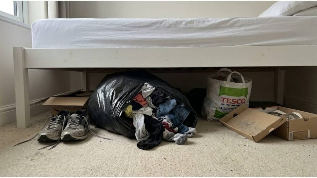 Clothes, shoes and bags stored untidily under a bed in a small rental bedroom.