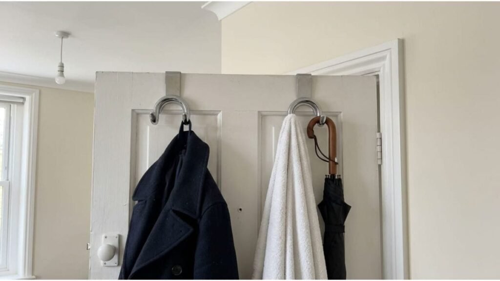 Over-the-door metal hooks holding a coat and umbrella in a small rental bedroom.