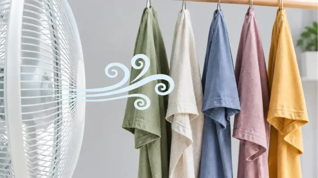 Desk fan blowing air across t-shirts hanging on a rail to help clothes dry faster indoors