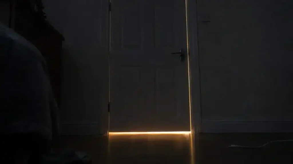Light shining through the gaps under and beside a bedroom door in a dark room, showing where sound can leak