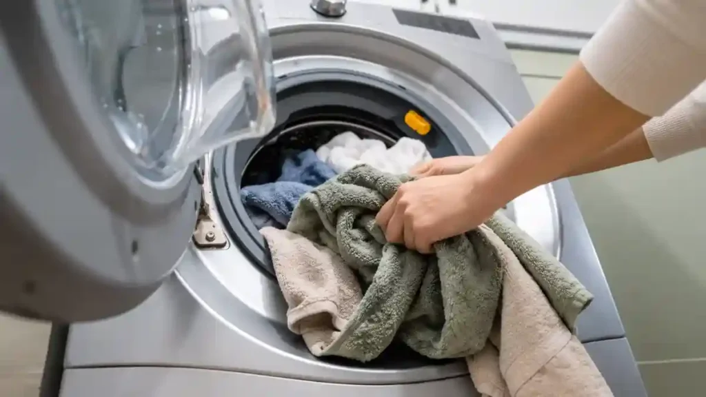 Hand pulling wet towels out of a washing machine drum straight after the cycle finishes, to start drying clothes quickly